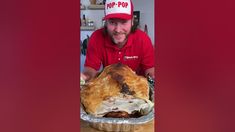 a man in a red shirt is holding a large roast beef pie