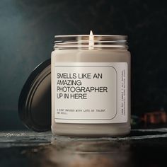 a candle sitting on top of a table next to a jar filled with something that says smells like an amazing photographer up in here