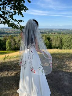 a woman in a white wedding dress and veil looking out at the countryside from behind