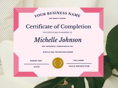 a pink and gold certificate is on top of a white table with green leaves in front of it