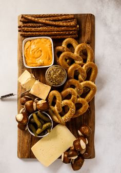 an assortment of pretzels, cheese and dips on a wooden cutting board