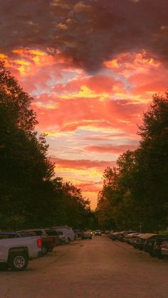 a parking lot filled with lots of parked cars under a colorful sky at sunset or sunrise