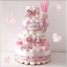 a pink and white baby shower cake with bunny decorations on the top is surrounded by hearts