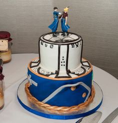 there is a wedding cake with two people on top and blue ribbon around the bottom