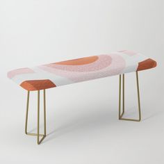 a pink and orange bench with gold legs on a white background in front of a wall