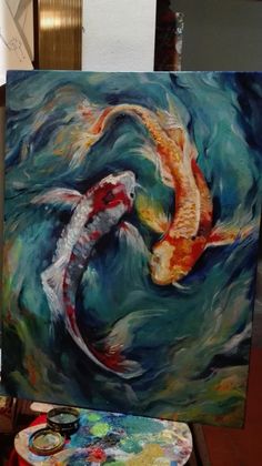 a painting of two koi fish in the water with paintbrushes on easel