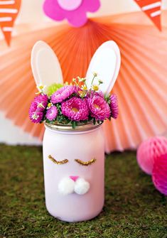 a mason jar with flowers and bunny ears painted on the side, sitting in grass