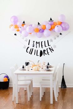 a white table topped with lots of purple and orange balloons next to a black and white wall