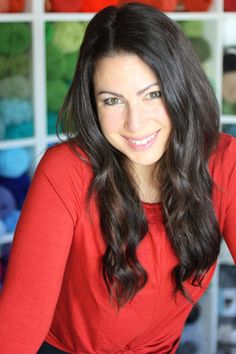 a woman in a red shirt is smiling at the camera and she has long dark hair