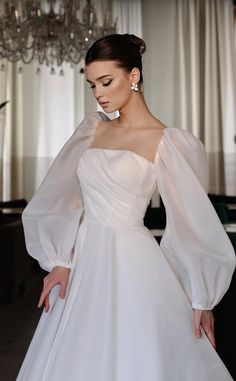 a woman in a white wedding dress standing next to a chandelier