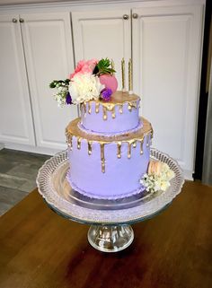 a three tiered cake with flowers and dripping icing on the top is sitting on a glass platter