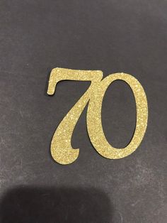 the number seventy is made out of gold glitter and sits on top of a black surface