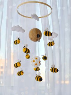 a baby mobile with bees and flowers hanging from it's sides in front of a window