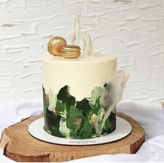 a wedding cake decorated with green leaves and gold decorations on a white plate next to a wooden slice