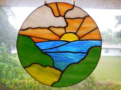 a round stained glass window with the sun setting over a lake and mountains in it