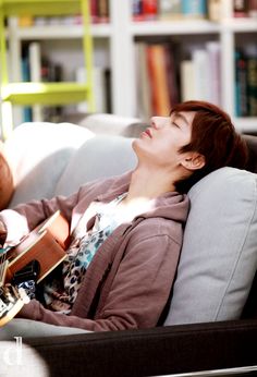 a woman laying on top of a couch next to a book shelf holding a guitar