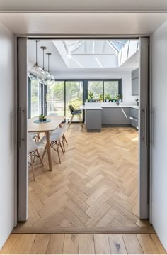 an open door leading to a kitchen and dining area with wooden floors, white walls and windows