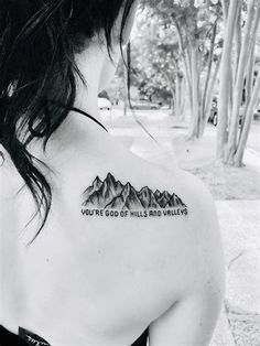 the back of a woman's shoulder with mountains on it and words written in black ink