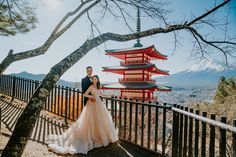 a bride and groom standing in front of a tall red pagoda on top of a hill