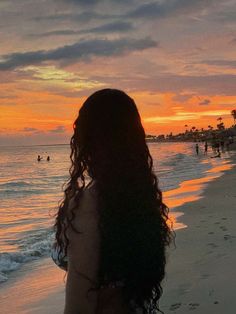 the back of a woman's head as she stands on the beach at sunset