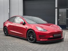 a red tesla model 3 parked in front of a garage door with black rims