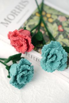 two small crocheted flowers sitting on top of a book next to each other