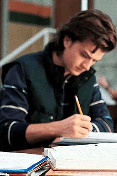 a man sitting at a desk writing on a piece of paper with a pencil in his mouth