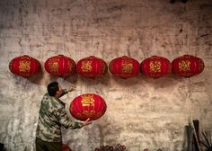 a man standing next to a wall with red lanterns hanging from it