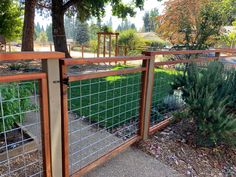 a fenced in area with plants and trees on the other side, surrounded by grass