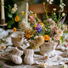 a table topped with lots of flowers and knitted slippers next to a vase filled with wildflowers