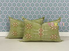 two green pillows sitting on top of a floor next to a blue and white wall