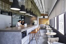 two people are sitting at the bar in an office with high ceilings and hanging plants