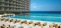 an outdoor swimming pool with lounge chairs and the ocean in the backgrouds