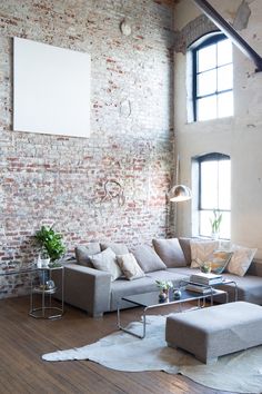 a living room filled with lots of furniture next to a tall brick wall and windows