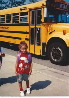 two children standing in front of a yellow school bus