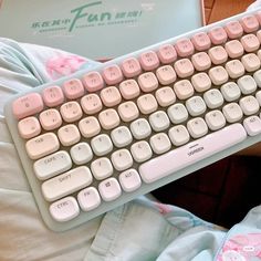 a white keyboard with pink keys sitting on top of a person's lap next to a book