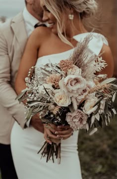 a bride and groom standing together with their bouquet