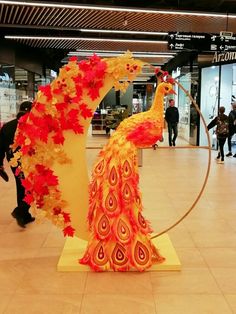 a sculpture of two peacocks with red leaves on their heads and tails, in the middle of an airport lobby