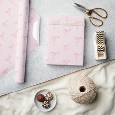 a table topped with pink wrapping paper next to scissors and balls of yarn on top of a white surface