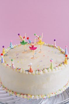 a birthday cake with white frosting and colorful decorations on the top is sitting on a glass platter