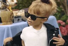 a young boy wearing sunglasses and holding a cell phone in front of a table with other items on it