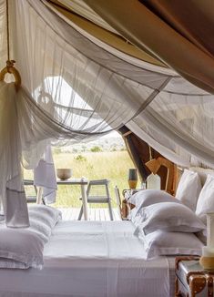 a bed with white sheets and pillows in a room that looks out onto the field