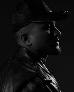 a black and white photo of a man in a leather jacket wearing a baseball cap