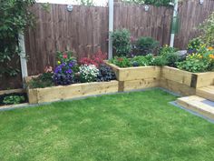 an outdoor garden with wooden raised planters and flowers in the center, surrounded by green grass