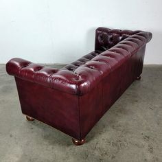 a red leather couch sitting on top of a cement floor next to a white wall