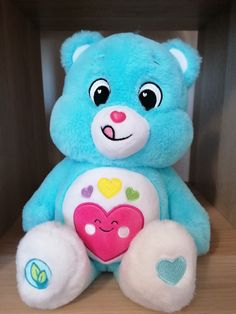 a blue teddy bear with hearts on it's chest sitting in front of a wooden shelf