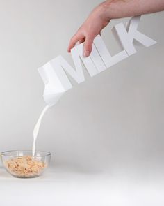 a person pouring milk into a bowl with cereal and orange juice in front of them