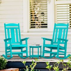 two blue rocking chairs sitting next to each other on a porch in front of a white house