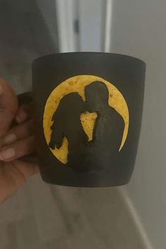 a person holding up a black and yellow coffee mug with the silhouette of two people