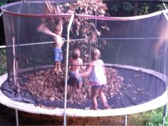 three children playing in a trampoline with leaves on the ground